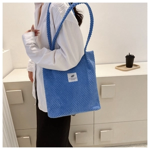 Blue corduroy shoulder bag with 'You need this one' label shown on model in soft light