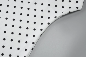 Close-up detail of smooth white fabric with classic black polka dots on summer dress