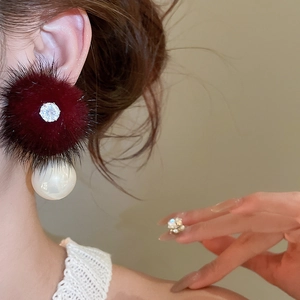 Macro shot of stylish gold-plated earrings with burgundy fur pom-poms and white pearls