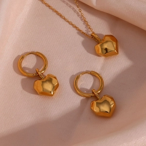 Polished gold heart pendant necklace and matching hoop earrings on pink satin background