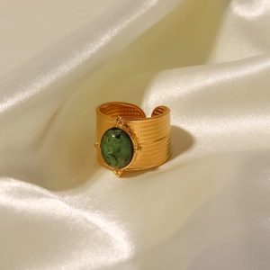 Detail of wide 18K gold stainless steel ring with a large oval green stone on beige silk