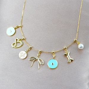 Gold-finish multi-pendant necklace with heart, bow, and bone charms on beige silk