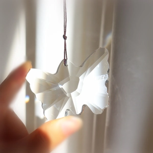Hand holding a crystal butterfly suncatcher prism with light refraction and red string