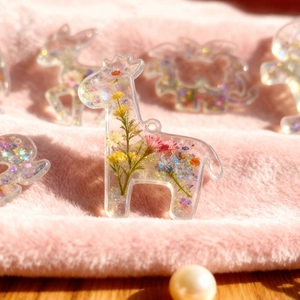 Vue détaillée d'un pendentif girafe en résine avec fleurs séchées et paillettes colorées