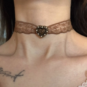 Gros plan d'un tour de cou en dentelle marron avec pendentif cœur et perle sur mannequin