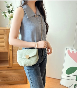 Détail d'un sac besace vert clair avec fermoir coeur doré et bandoulière chaîne