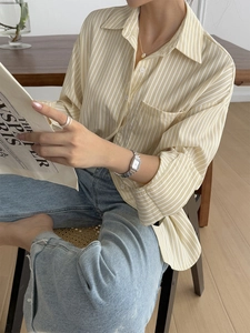 Vertical yellow and white striped long sleeve shirt with model reading in a casual setting