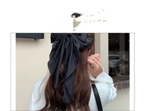 Elegant large black satin bow hair clip with long ribbons styled on long wavy brown hair