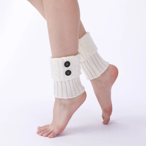Close-up of cream knit leg warmers featuring cable patterns and black button details
