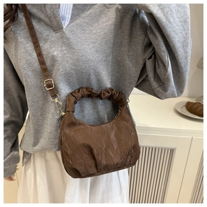 Detail of brown pleated crescent handbag with golden hardware and textured cloud finish