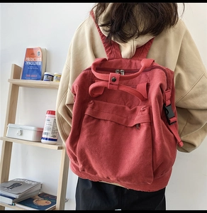 Red canvas backpack detail showing side buckles and front pocket in a lifestyle setting