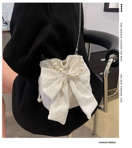 Detail of cream white crossbody bag with bow, pearl handle, and floral jacquard texture