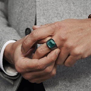 Close-up of men's square green gemstone ring with dark gunmetal band on suit background