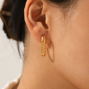 Close-up of a gold twisted C-shape hoop earring featuring woven texture on a model