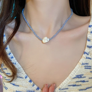 Close-up of a light blue beaded necklace with a white heart stone on a model's neck