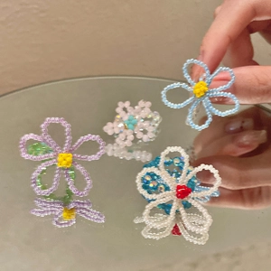 Détail de bagues fleurs en perles faites main aux tons pastels avec reflet de miroir