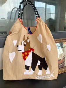 Beige canvas tote bag with dog embroidery, heart applique and rope handles shown on display