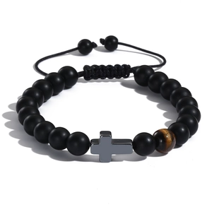 Dettaglio del bracciale intrecciato con perle nere opache, occhio di tigre e croce