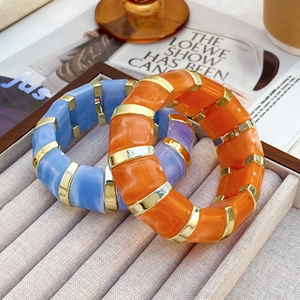 Makro-Detail von klobigen Harz-Armreifen in Orange und Graublau mit Gold-Trennelementen
