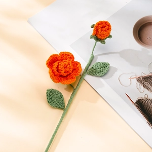 Detailed close-up of handmade crochet orange rose with green leaves on book background