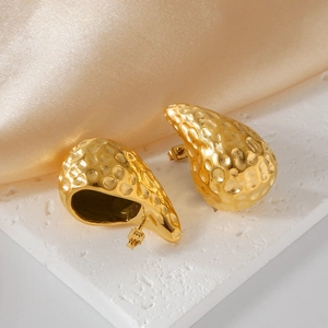 Macro shot of gold teardrop earrings with hammered texture on silk fabric background