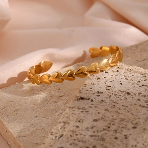 Detail of gold heart-shaped adjustable open cuff bracelet on a stone and silk background