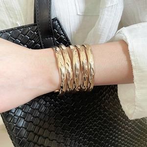 Detailed view of five hammered gold bangles styled with a white shirt and black woven bag