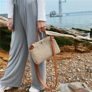 Detailed view of straw woven bag with brown leather trim and golden twist lock closure