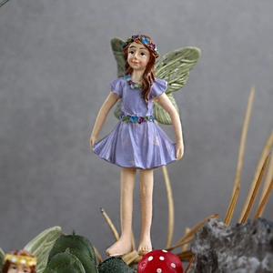 Close-up of resin flower fairy figurine with purple dress and green wings in micro landscape