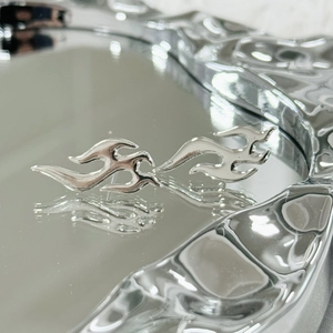Macro detail of polished stainless steel flame stud earrings with high-shine mirror finish