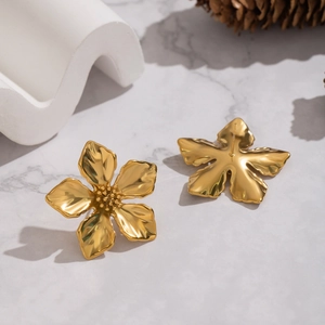Close-up of golden flower stud earrings with detailed petals on marble surface