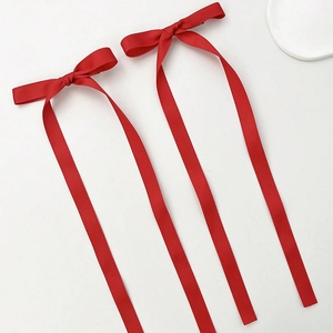 Detail of two red satin ribbon bow hair clips with a glossy finish on white background