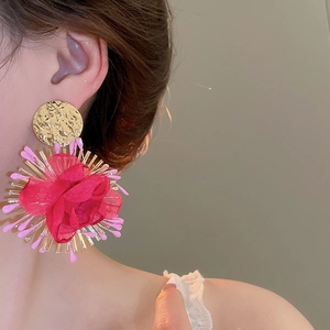 Detailed view of model wearing a large red chiffon flower earring with gold textured base