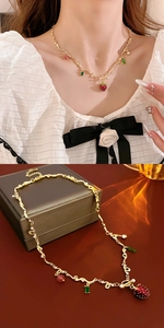 Detail of gold strawberry glass necklace with green gemstone and beaded accents on model