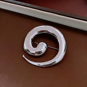 Minimalist silver spiral metal brooch with mirror finish on dark leather background