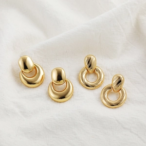 Detailed close-up of 18K gold hollow geometric stud earrings on white textured fabric