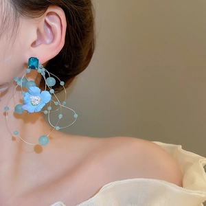 Close-up of blue floral tassel earrings with glass beads worn on model against beige background