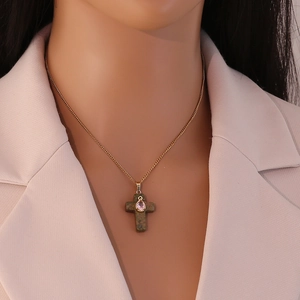Close-up of golden cross necklace with green stone and pink teardrop gemstone