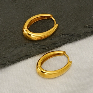 Polished gold stainless steel oval hoop earrings on a stone and fabric background