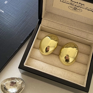 Close-up of chunky gold oval stud earrings presented in a luxury black jewelry box
