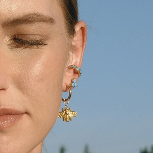 Close-up of a woman wearing gold bee earrings and turquoise flower studs against blue sky