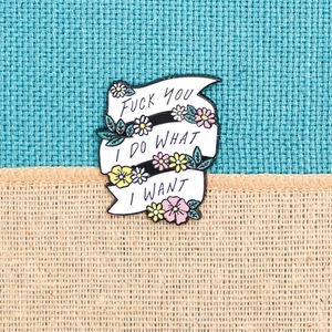 Enamel pin with white ribbon and flowers reading Fuck You I Do What I Want