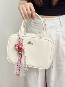 Detail van beige handtas met rode geruite strik en kanten lint accessoire