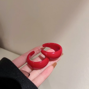 Close-up of glossy red C-shaped hoop earrings showcasing the smooth texture and size