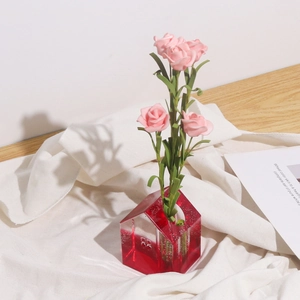 Dettaglio del vaso in resina rossa a forma di casa con rose rosa su sfondo in tessuto bianco