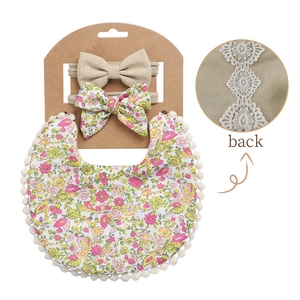 Detail view of cotton floral baby bib with pom-pom trim and lace back embroidery