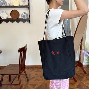 Detailed shot of black canvas tote with red butterfly embroidery and woven rope handles