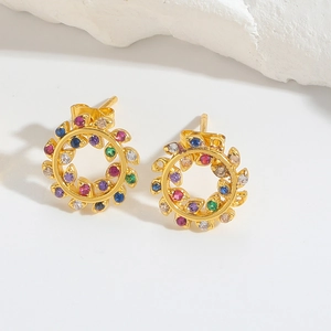 Detailed close-up of gold stud earrings with colorful zircons on a white stone background