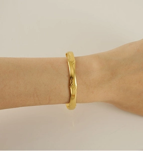 Detailed close-up of a gold-plated bamboo style bangle bracelet on a model wrist
