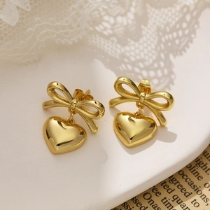 Macro detail of gold plated bow and heart pendant earrings on a white stone pedestal
